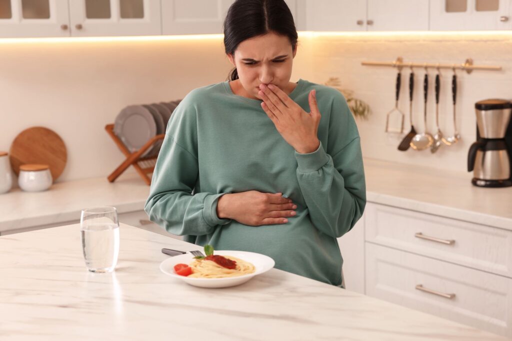 Young woman feeling nausea while seeing food at table in kitchen.